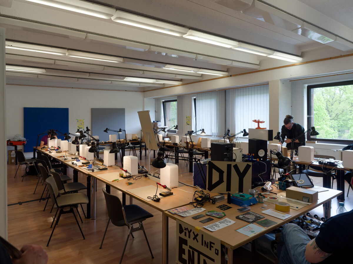 Soldering stations set up in the SUPERBOOTH DIY area: long tables with soldering irons, desk lamps and tools