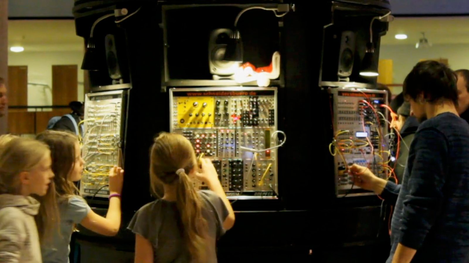 Children and an adult patching cables at HerrSchneider's Synthesizer Carousel, a round unit housing modular systems and speakers